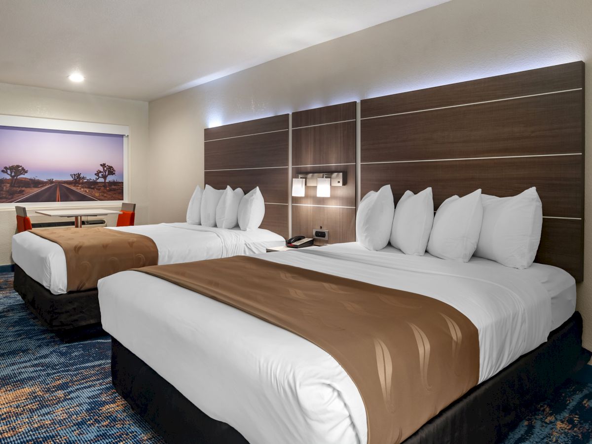 The image shows a hotel room with two neatly made double beds, modern headboards, a window, and artwork on the wall, creating a cozy atmosphere.