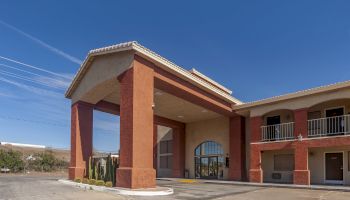 The image shows the exterior of a building with a large covered entryway, featuring an arched window and multiple balconies.