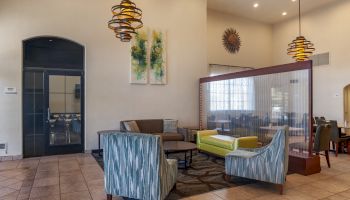 The image shows a modern lounge area with sofas, armchairs, decorative wall art, pendant lights, and a partition wall, in a well-lit environment.