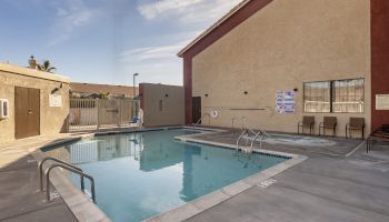 The image shows an outdoor pool area beside a building, with metal railings, pool chairs, and safety signs visible.