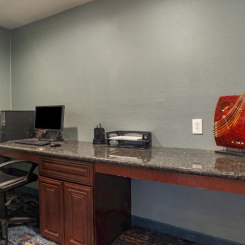 The image depicts a home office setup with a desk, chair, computer, printer, and decorative objects including a globe and red sculpture on a granite surface.