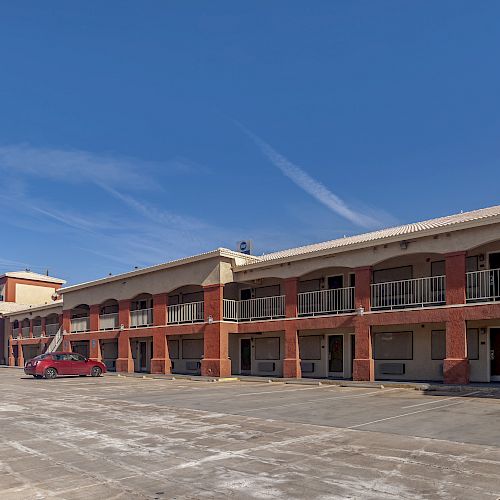 The image shows a two-story motel with a red exterior, an empty parking lot, and a single red car parked outside.