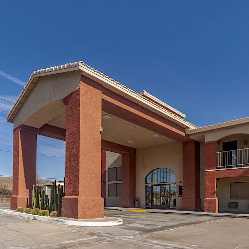 An image of a two-story building with a large entrance canopy, possibly a hotel or motel, under a clear blue sky and surrounded by a paved area.