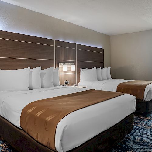 A modern hotel room with two double beds, brown and white bedding, a carpeted floor, and a bathroom area in the background ending the sentence.