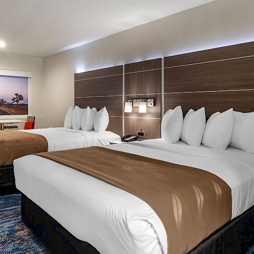 The image shows a hotel room with two neatly made beds, each with white linens and brown bed runners, along with a large wall painting.