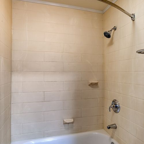 The image shows a bathroom with a tiled shower area, a showerhead, a bathtub, soap holders, and a metal shelf.