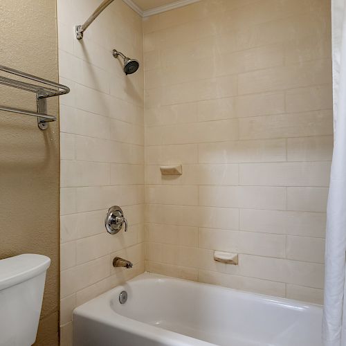 This image shows a bathroom with a bathtub, showerhead, white shower curtain, towel rack, and toilet.