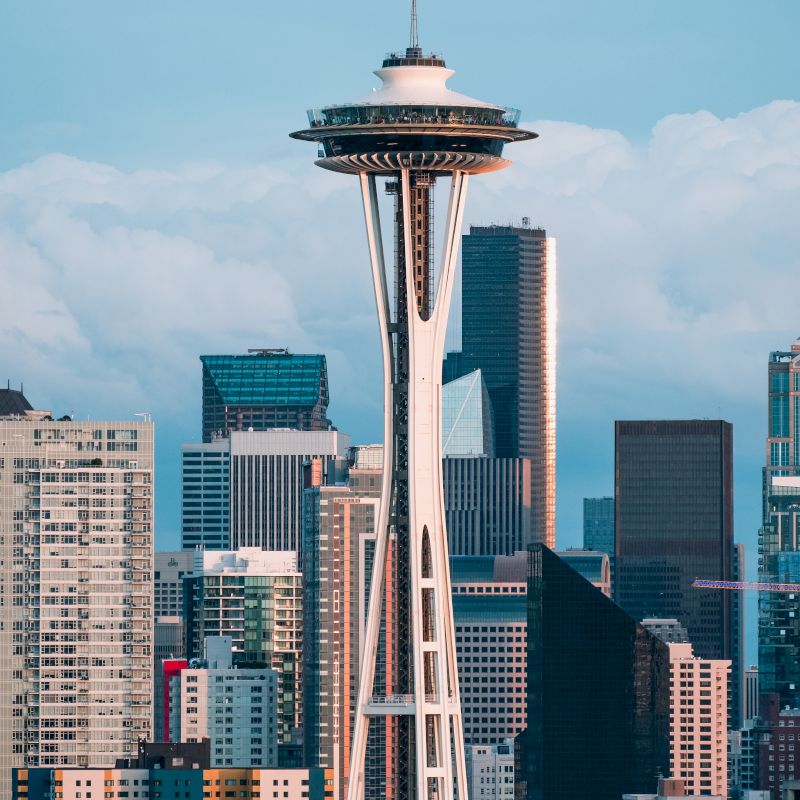 The image shows an iconic observation tower set against a backdrop of modern skyscrapers and a partly cloudy sky.