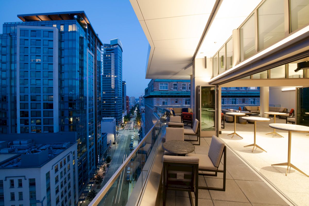 Modern outdoor terrace with seating overlooking a cityscape with high-rise buildings at dusk.