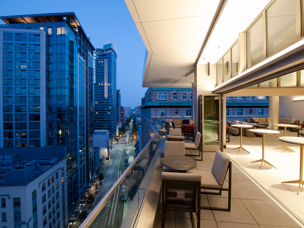 Modern outdoor terrace with seating overlooking a cityscape with high-rise buildings at dusk.