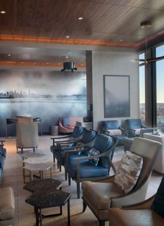 A lounge with modern seating, large windows offering ocean views, and a mural of a city skyline on the wall.