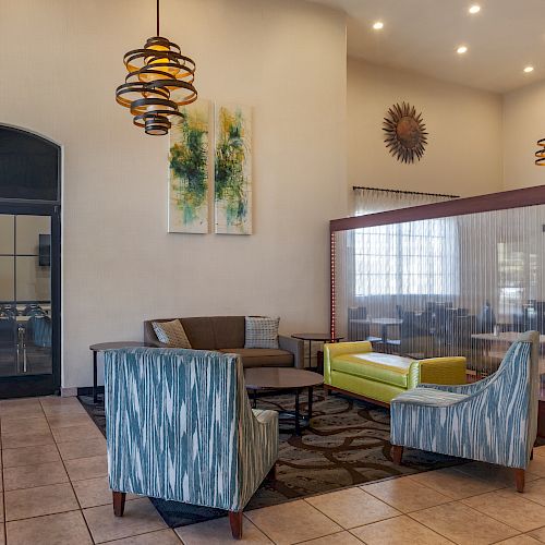 This image shows a modern lounge area with armchairs, a sofa, pendant lights, and abstract wall art. There's a partition separating two spaces.